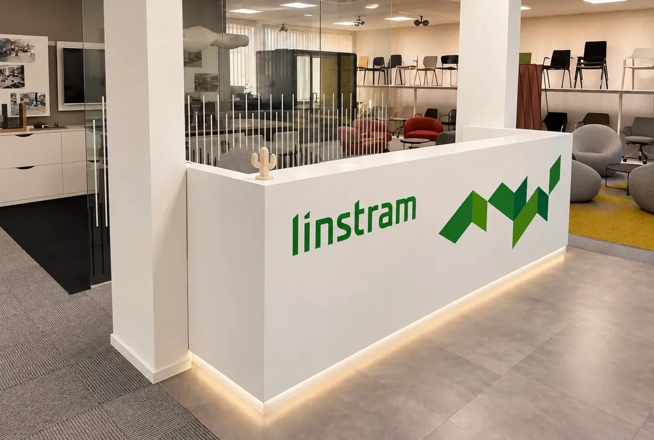 Recepce showroomu Worklab s logem Linstram z boku, v pozadí vystavené židle a šedá křesla na žlutém koberci